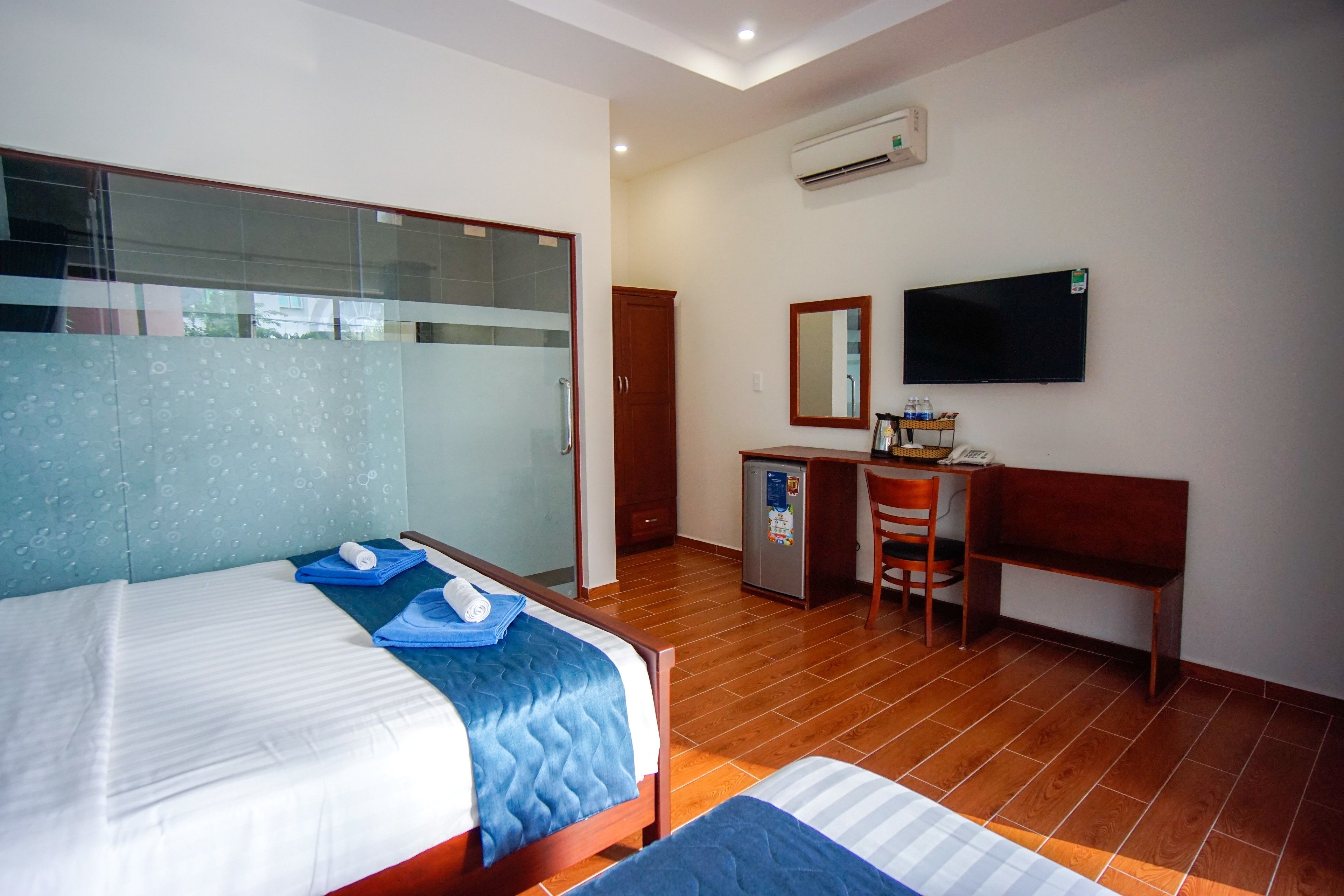 A hotel room with a bed, a desk with a chair, a television, and a small refrigerator.