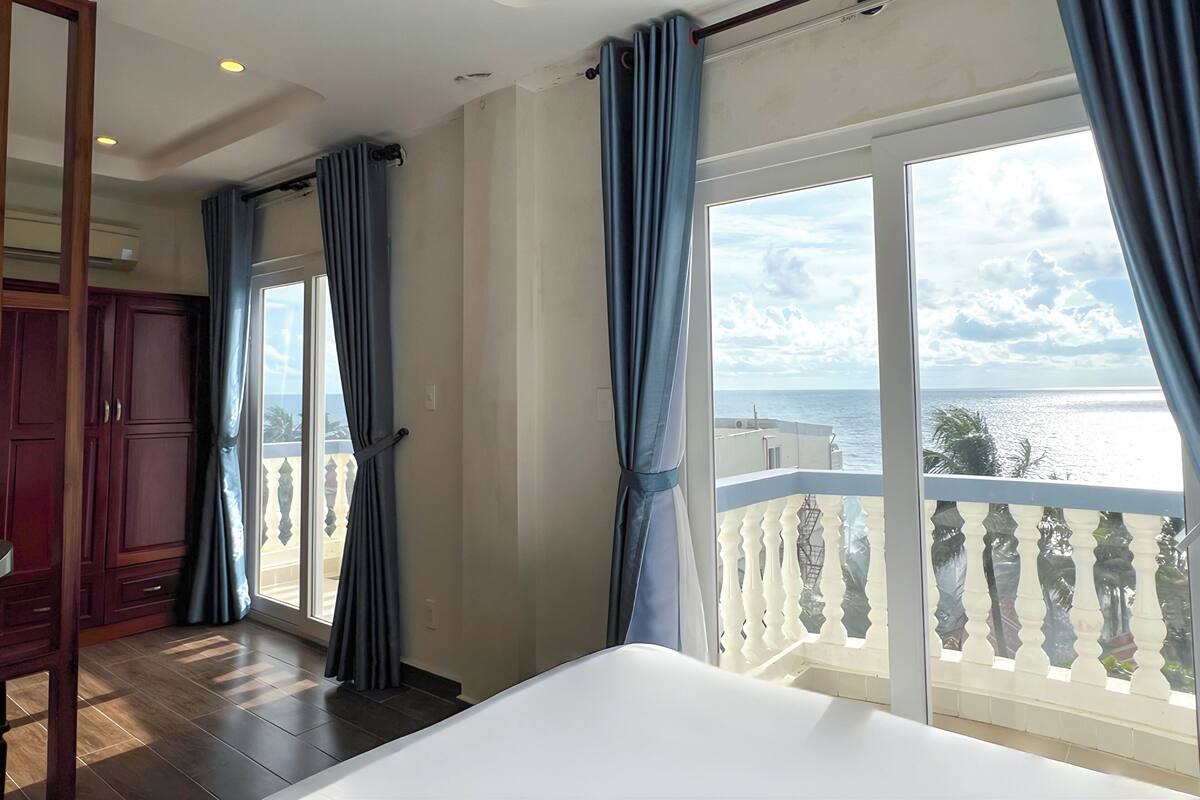 A hotel room with a large window, a bed, and a wooden wardrobe.