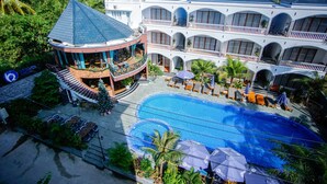 Un hotel de varios pisos con piscina, balcones y abundante vegetación.