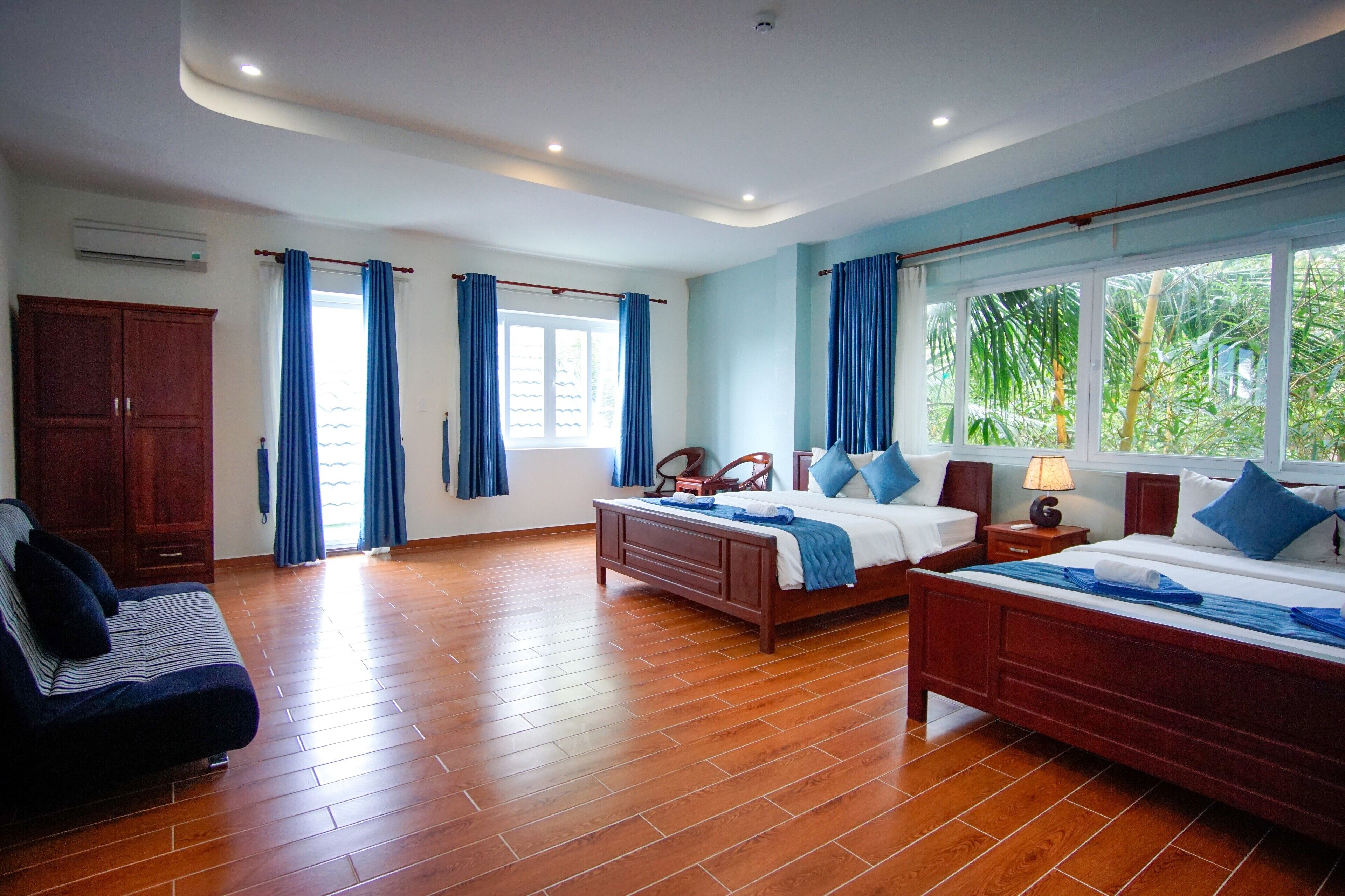 A spacious bedroom with two beds, a wooden wardrobe, and a sofa.