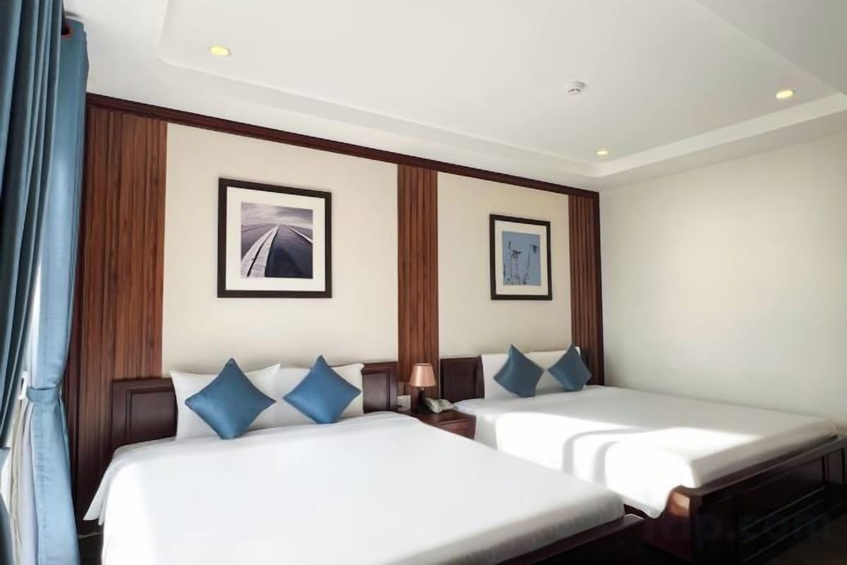 A hotel room with two single beds, a nightstand with a lamp, and a framed picture on the wall.