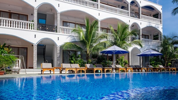 Un hotel con una piscina grande, varios balcones y sillones de descanso.
