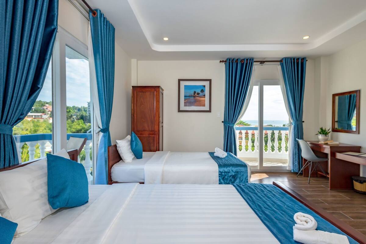 A hotel room with two beds, a desk, a chair, a wardrobe, and a balcony with a view.