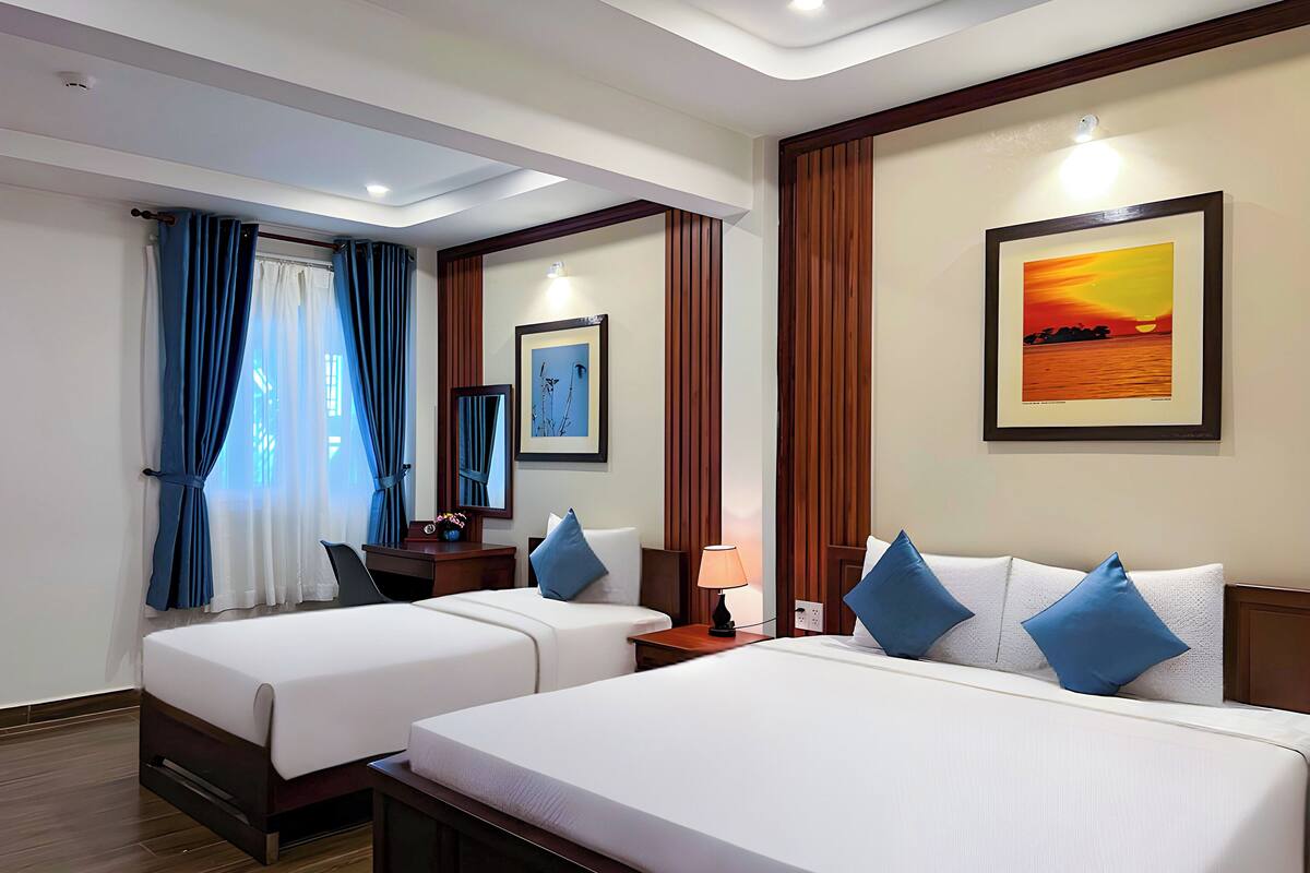 A hotel room with two beds, a desk, a chair, a lamp, and a framed picture on the wall.