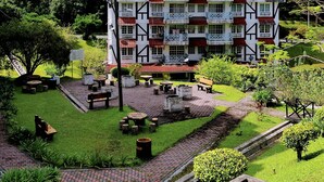 Ein mehrstöckiges Gebäude mit Balkonen, umgeben von einem gepflegten Garten mit Wegen, Bänken und einem kleinen Wasserspiel.