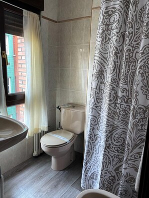 A bathroom with a toilet, a sink, and a window with curtains. - Hotel Ovetense (Oviedo)