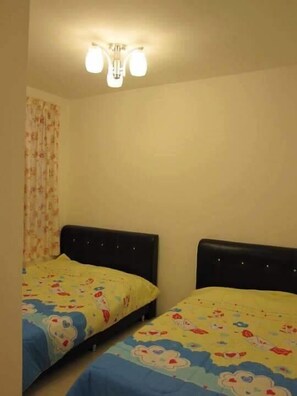 A room with two beds, each with a floral-patterned bedspread, a ceiling light fixture, and a floral curtain. - SA Apartments at Crown Imperial Court (Brinchang)