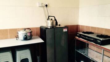 A compact kitchen with a refrigerator, a kettle, and a stove.