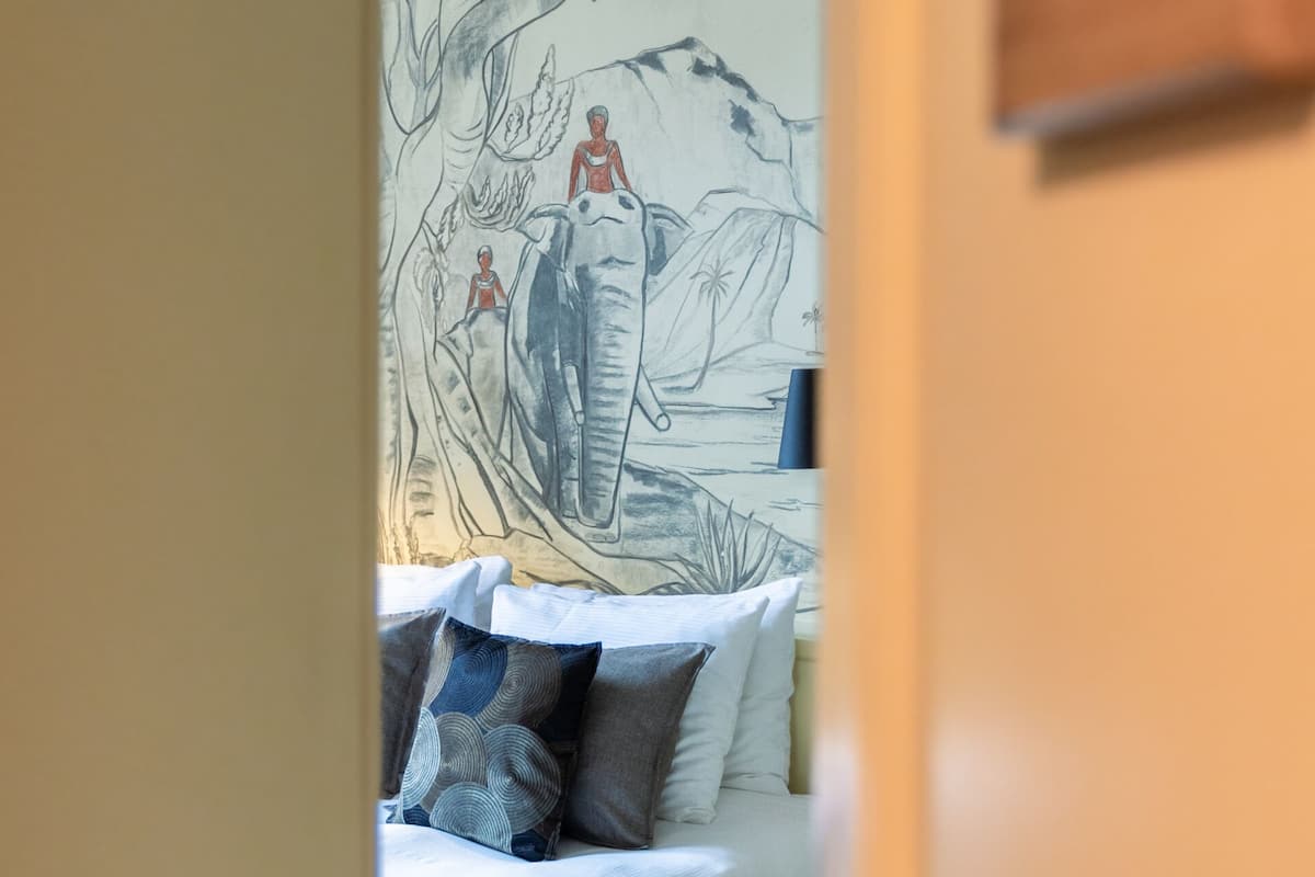 A bedroom with a bed, pillows, and a wall mural.