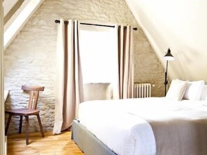 A bedroom with a bed, a chair, a lamp, and a window with curtains. - La Maison Pavie (Dinan)