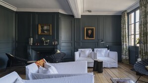 Une pièce avec une cheminée, des meubles blancs et une grande fenêtre avec des rideaux.