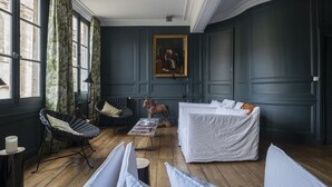 Une pièce avec une grande fenêtre, un lit, une chaise, une table et un tableau accroché au mur.