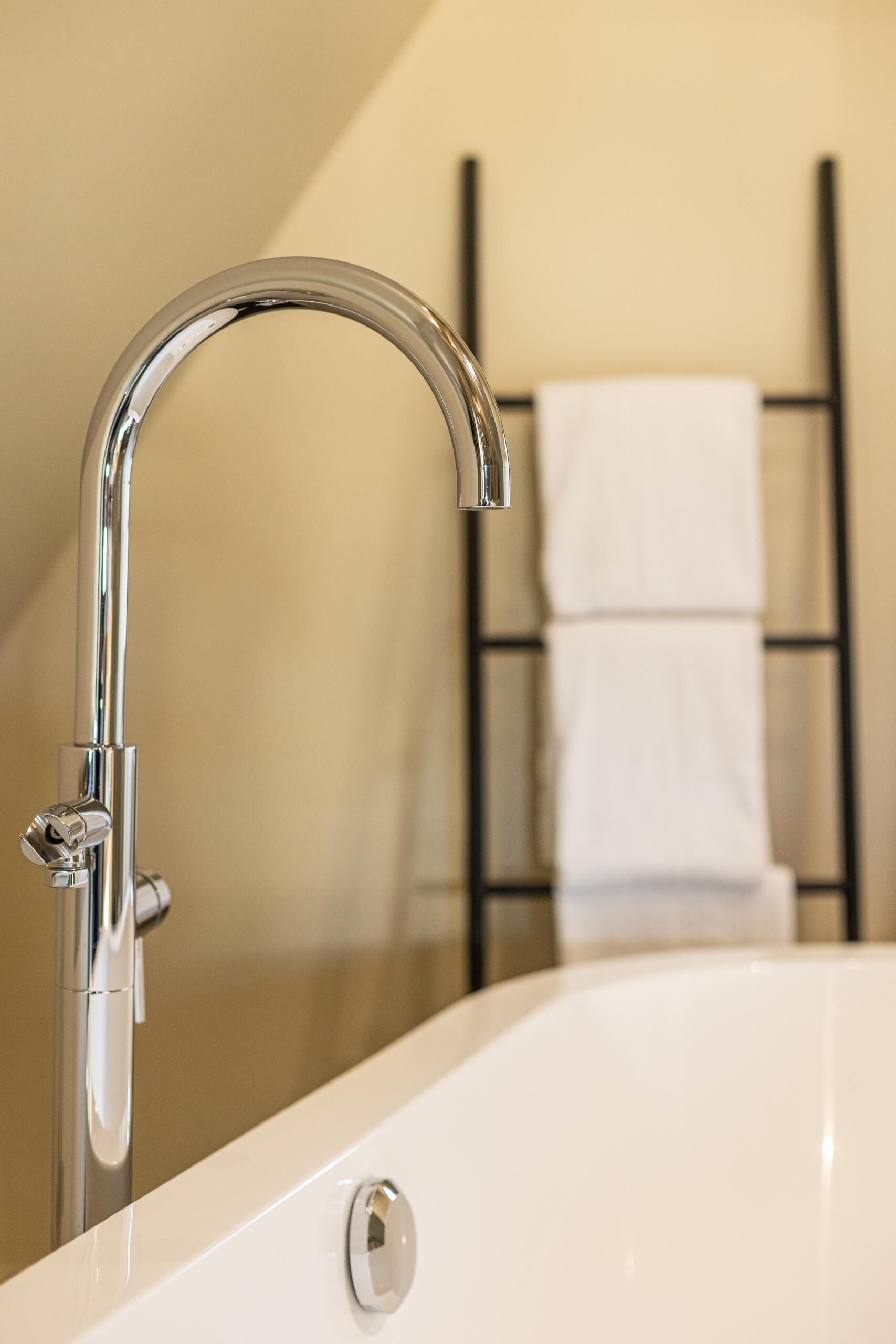 Ein modernes Badezimmer mit chromfarbenem Wasserhahn, einer weißen Badewanne und einem Handtuchhalter im Hintergrund.