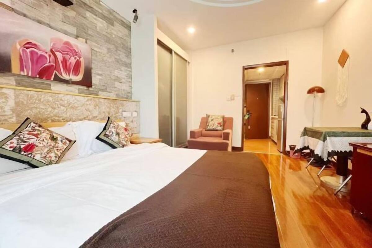 A hotel room with a bed, a chair, a table, and a door leading to another room.