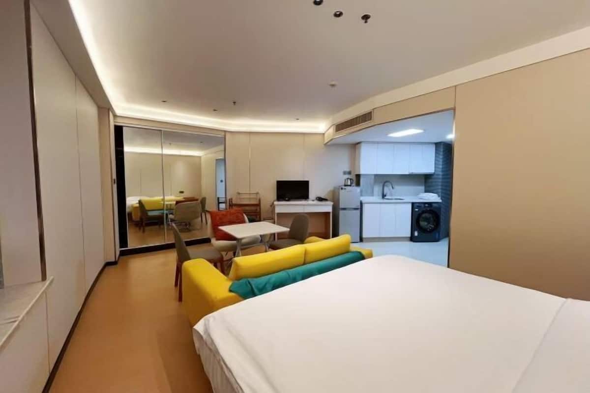 A modern hotel room with a bed, a small desk, a chair, and a sofa.