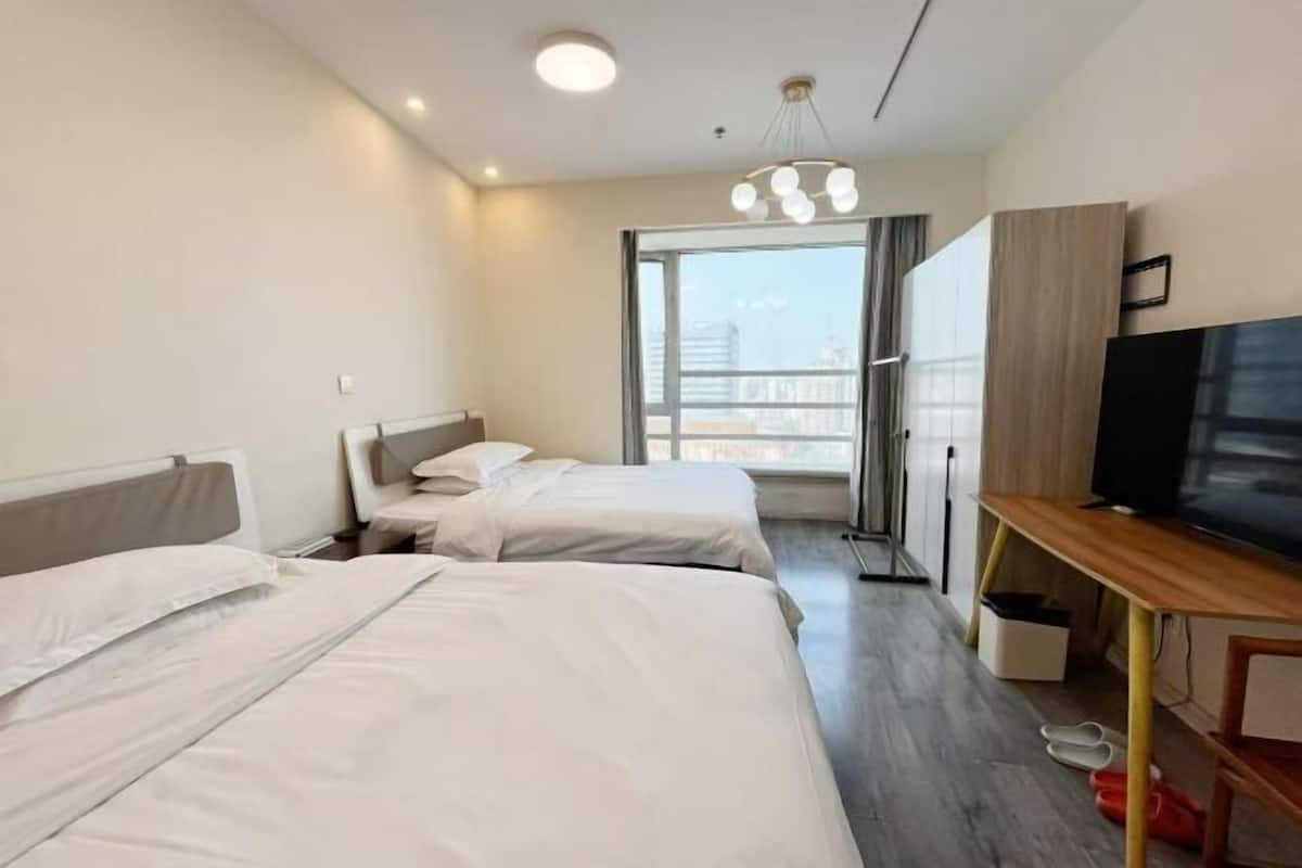 A hotel room with two beds, a TV, a wardrobe, and a balcony with a city view.