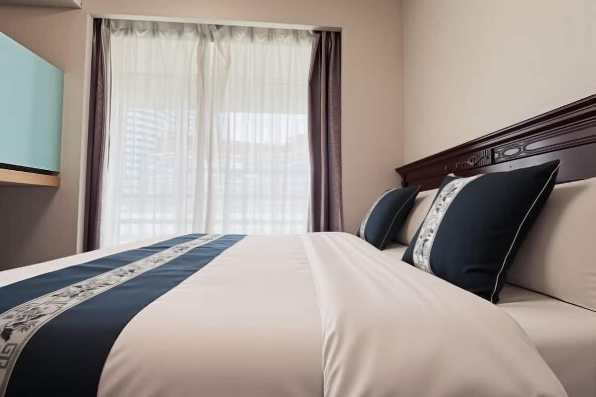 A hotel room with a bed, curtains, and a view of buildings.