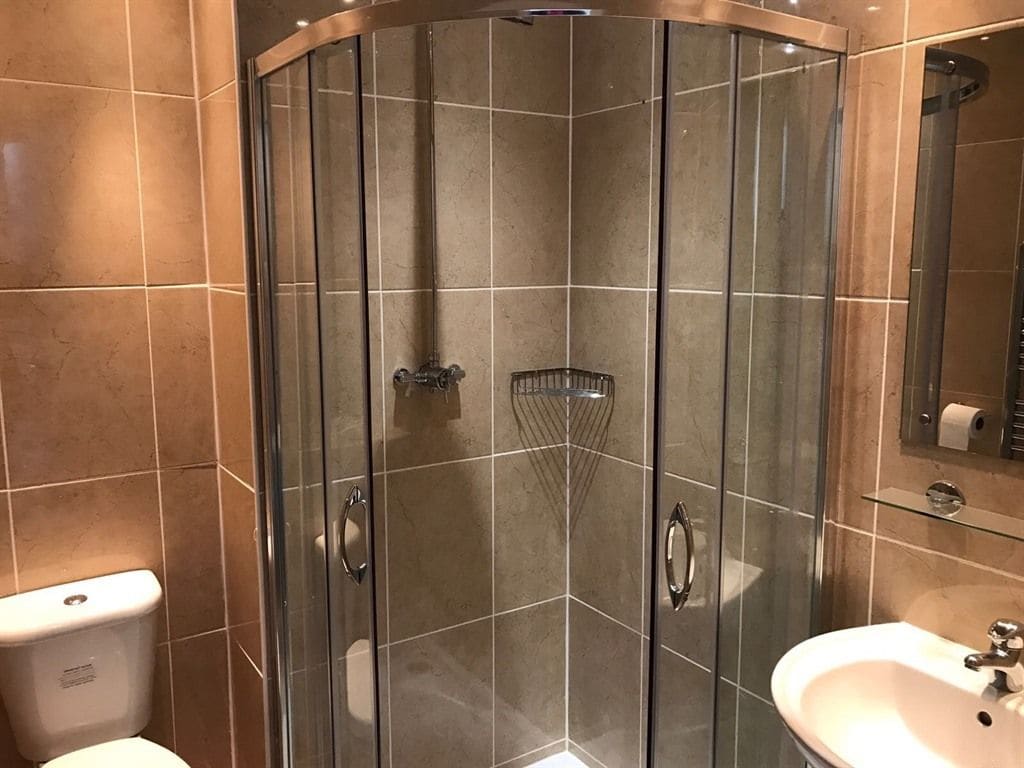 A corner bathroom with a glass-enclosed shower, a toilet, and a sink.