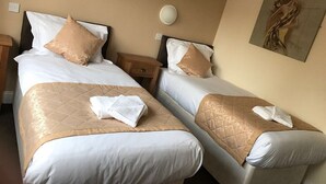 A hotel room with two beds, beige walls, and a painting on the wall.