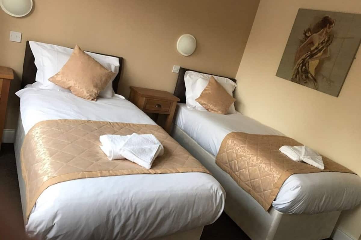 A hotel room with two beds, beige walls, and a painting on the wall.