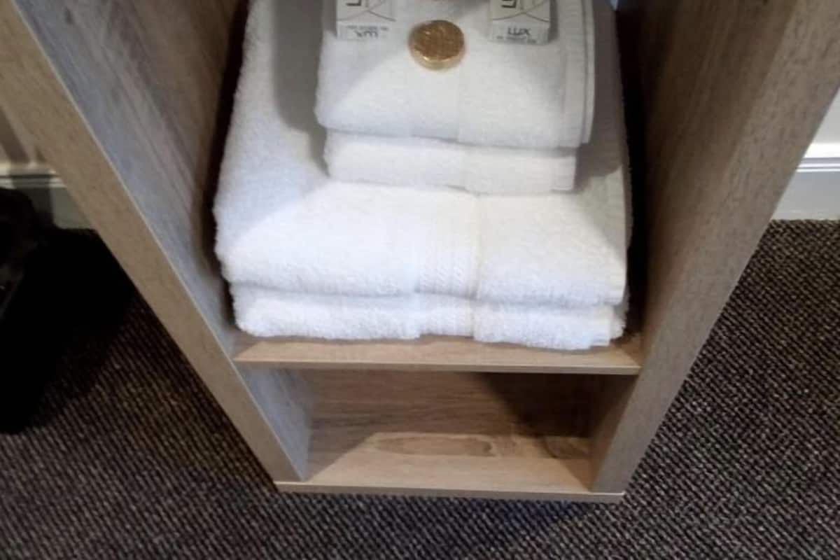 A wooden shelf with folded white towels and two Lux branded containers.