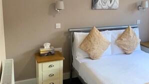 A hotel room with a bed, two wall-mounted lamps, a painting, and a bedside table with a tissue box.