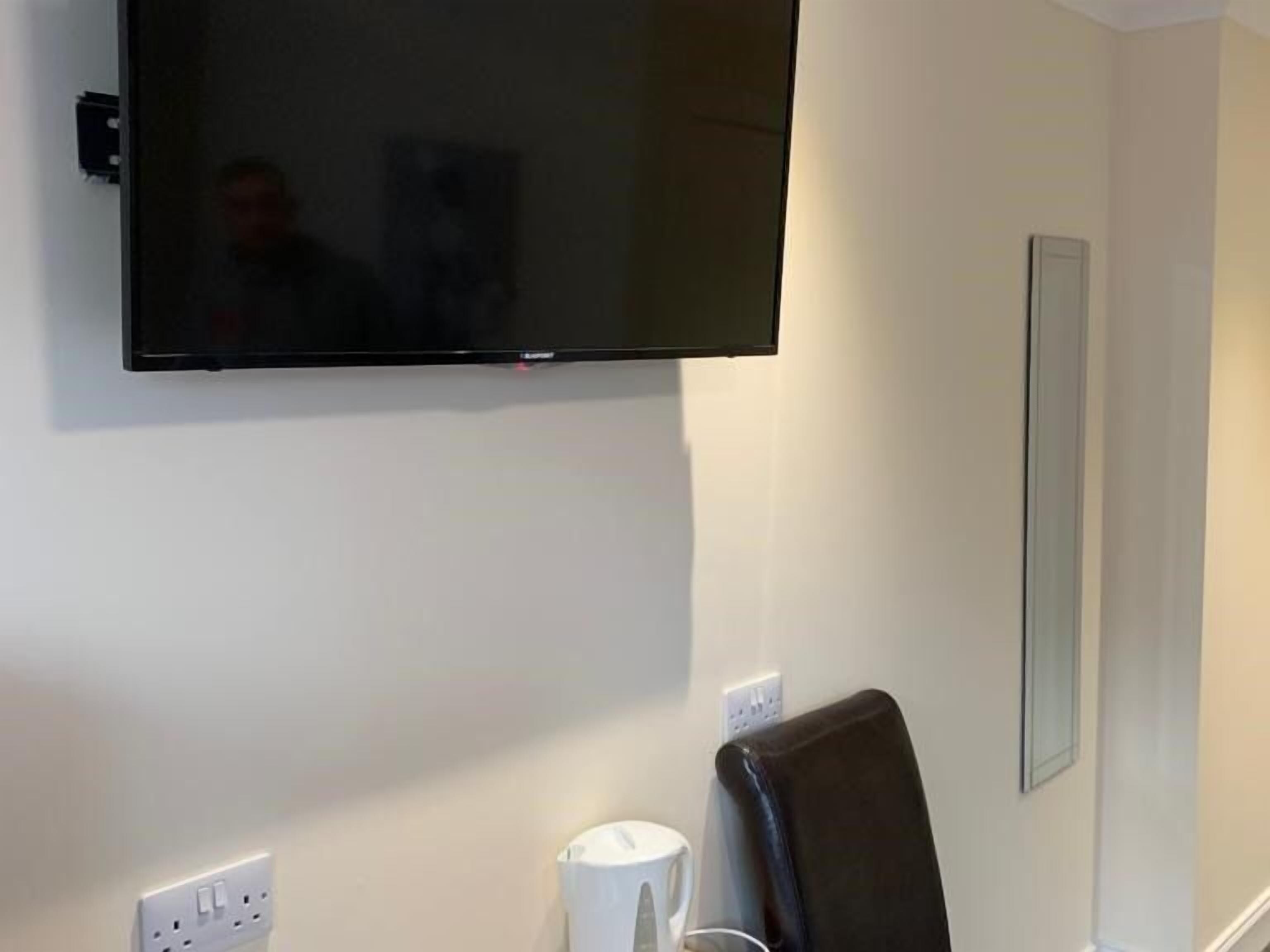 A flat-screen TV mounted on a wall, a white electrical outlet, and a black chair.