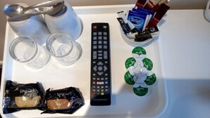 A tray with a remote control, two glasses, a bottle of milk, a pack of biscuits, and a container with various items. - Waverley Inn (Dingwall)