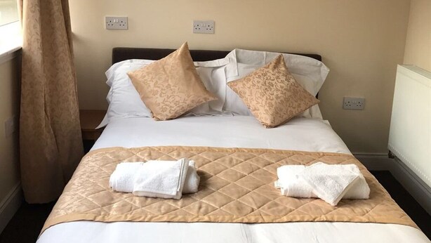 A neatly made bed with a quilted cover, two pillows, and two folded towels on the bed. - Waverley Inn (Dingwall)
