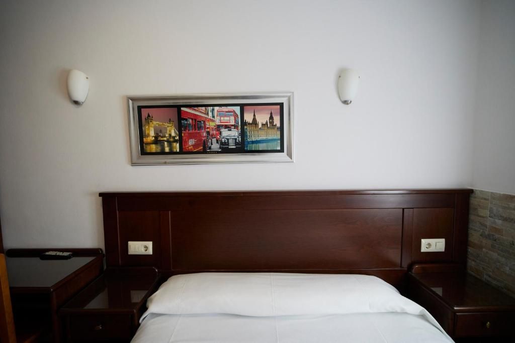 A hotel room with a large bed, a wooden headboard, two bedside tables, and a framed picture on the wall.
