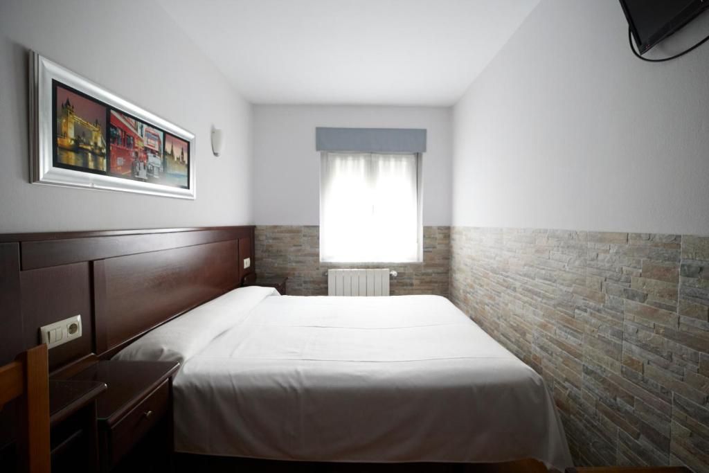 A hotel room with a single bed, a nightstand, a window with curtains, and a brick wall.