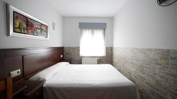 A hotel room with a single bed, a nightstand, a window with curtains, and a brick wall.