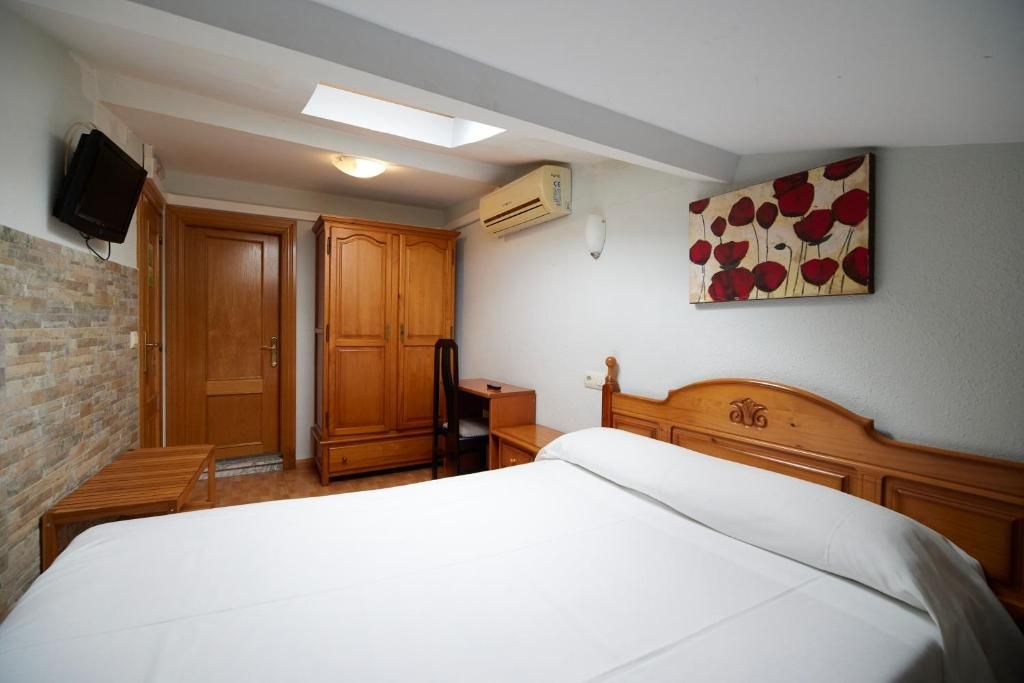 Une chambre à coucher avec un lit, une armoire en bois, un bureau et un téléviseur fixé au mur.