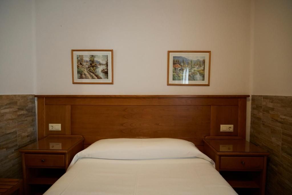 A hotel room with a wooden headboard, two bedside tables, and two framed landscape paintings on the wall.