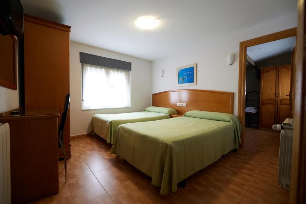 Une chambre avec deux lits, une fenêtre avec des rideaux, un radiateur et une porte donnant sur une autre pièce.