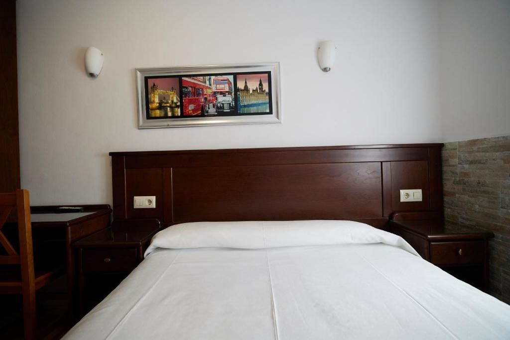 A hotel room with a large bed, a wooden headboard, a desk, and a chair. There is a framed picture on the wall above the bed.