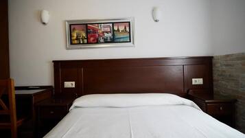 A hotel room with a large bed, a wooden headboard, a desk, and a chair. There is a framed picture on the wall above the bed.
