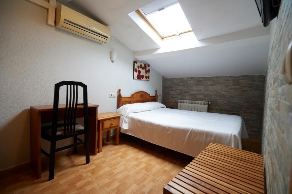 Un dormitorio con cama, escritorio, silla, tragaluz y radiador.