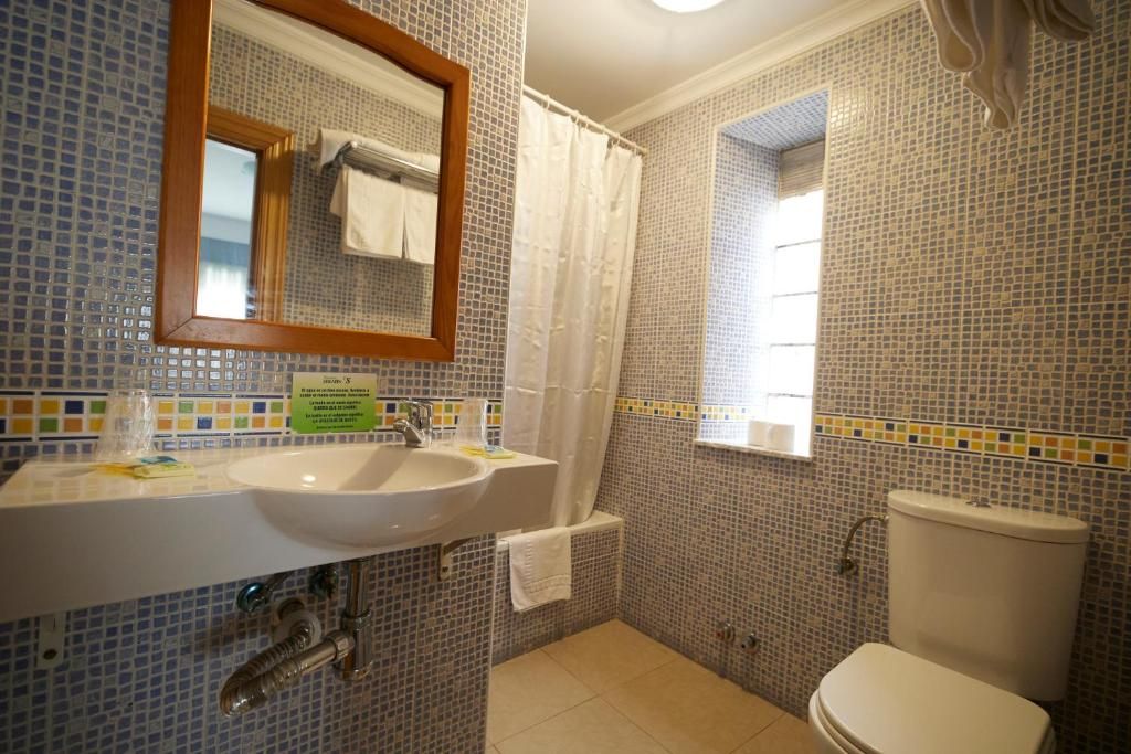 Un bagno con lavandino, specchio, water e finestra.