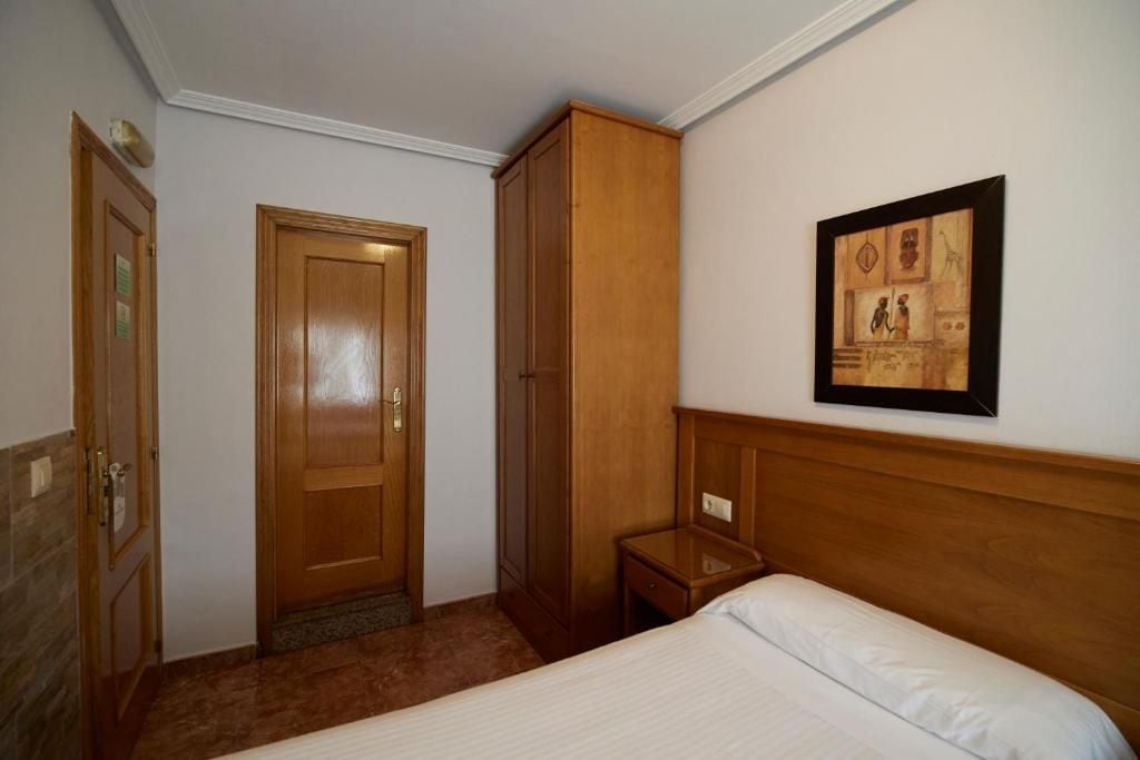 Een hotelkamer met een bed, een kledingkast, een nachtkastje en een lijst met een afbeelding aan de muur.