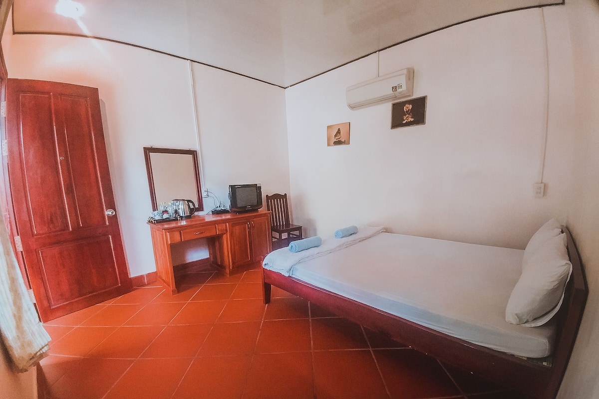A room with a bed, a desk with a television, a mirror, and a wardrobe.