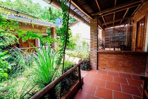 A covered patio with a brick wall, wooden railing, and potted plants.