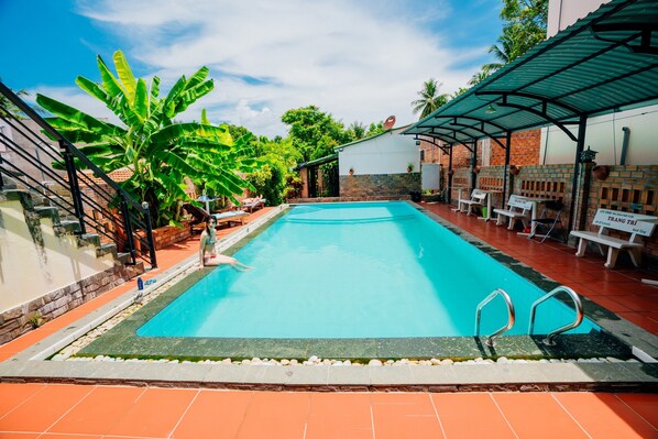 A swimming pool with a tiled deck, surrounded by lounge chairs and a covered seating area.