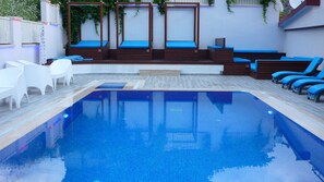 Una piscina al aire libre, sombrillas, sillones reclinables de piscina