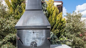 Una parrilla de carbón con chimenea, ubicada sobre una plataforma de piedra rodeada de piedras y follaje.