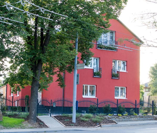 A red building with multiple windows, a black metal fence, and a tree in front.