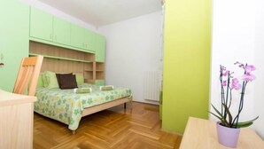 Un dormitorio con cama, una silla de madera, una mesita, una orquídea en maceta y armarios verdes.