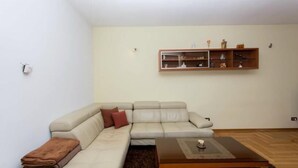 Una sala de estar con un sofá seccional color beige, una mesita de madera y un estante de pared con adornos.