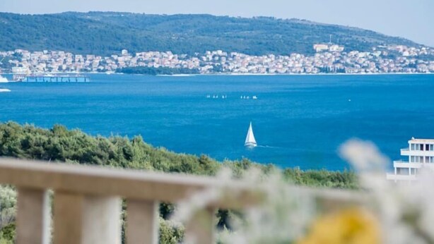 Un paisaje costero urbano con una vista despejada del mar, un velero y una colina distante con edificios.