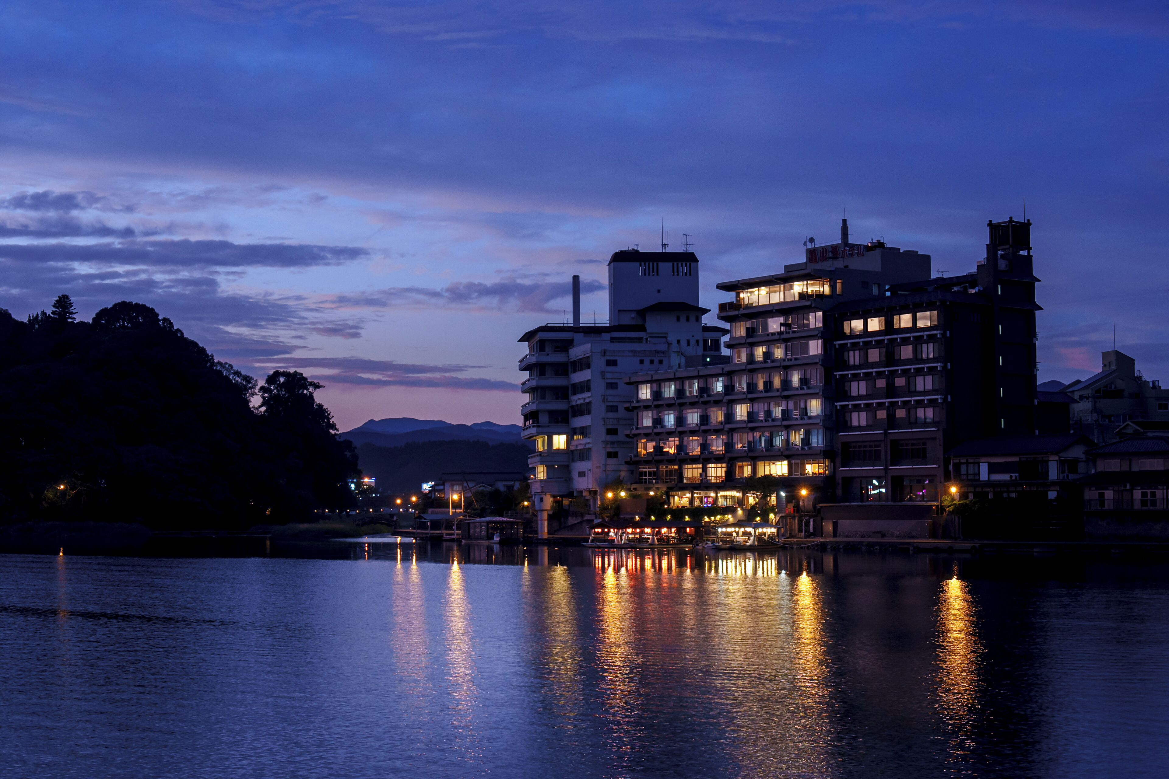 A multi-story hotel with balconies, located near a body of water reflecting lights.